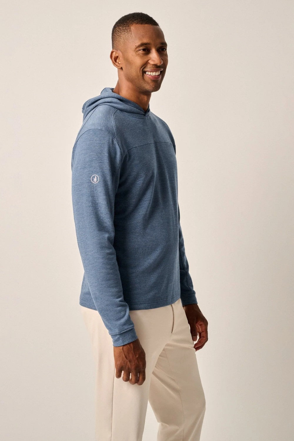 Man wearing a blue hoodie and beige pants on a plain background