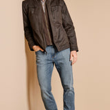 Man wearing a dark jacket, plaid shirt, and blue jeans against a beige background