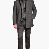 Man wearing a gray coat over a plaid shirt with gray pants on a white background