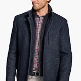 Man wearing a dark blue coat over a plaid shirt on a white background