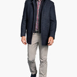 Man wearing a navy jacket, plaid shirt, and gray pants on a white background