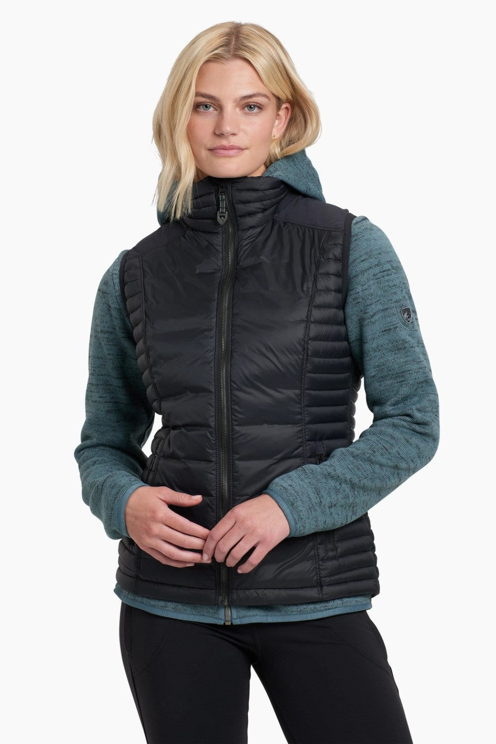 Woman wearing a black puffer vest over a teal sweater on a white background