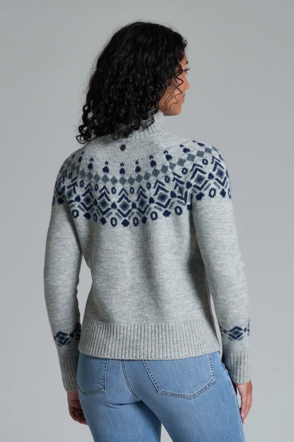 Woman wearing a gray sweater with blue patterned yoke against a gray background