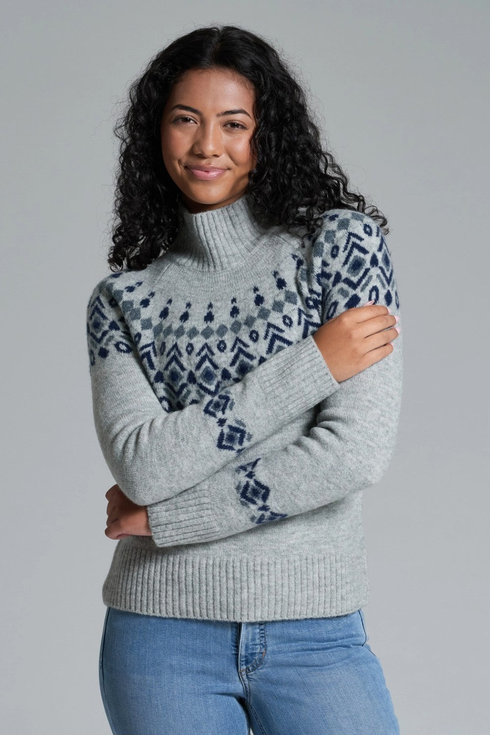 Woman wearing a gray sweater with patterned sleeves against a plain background