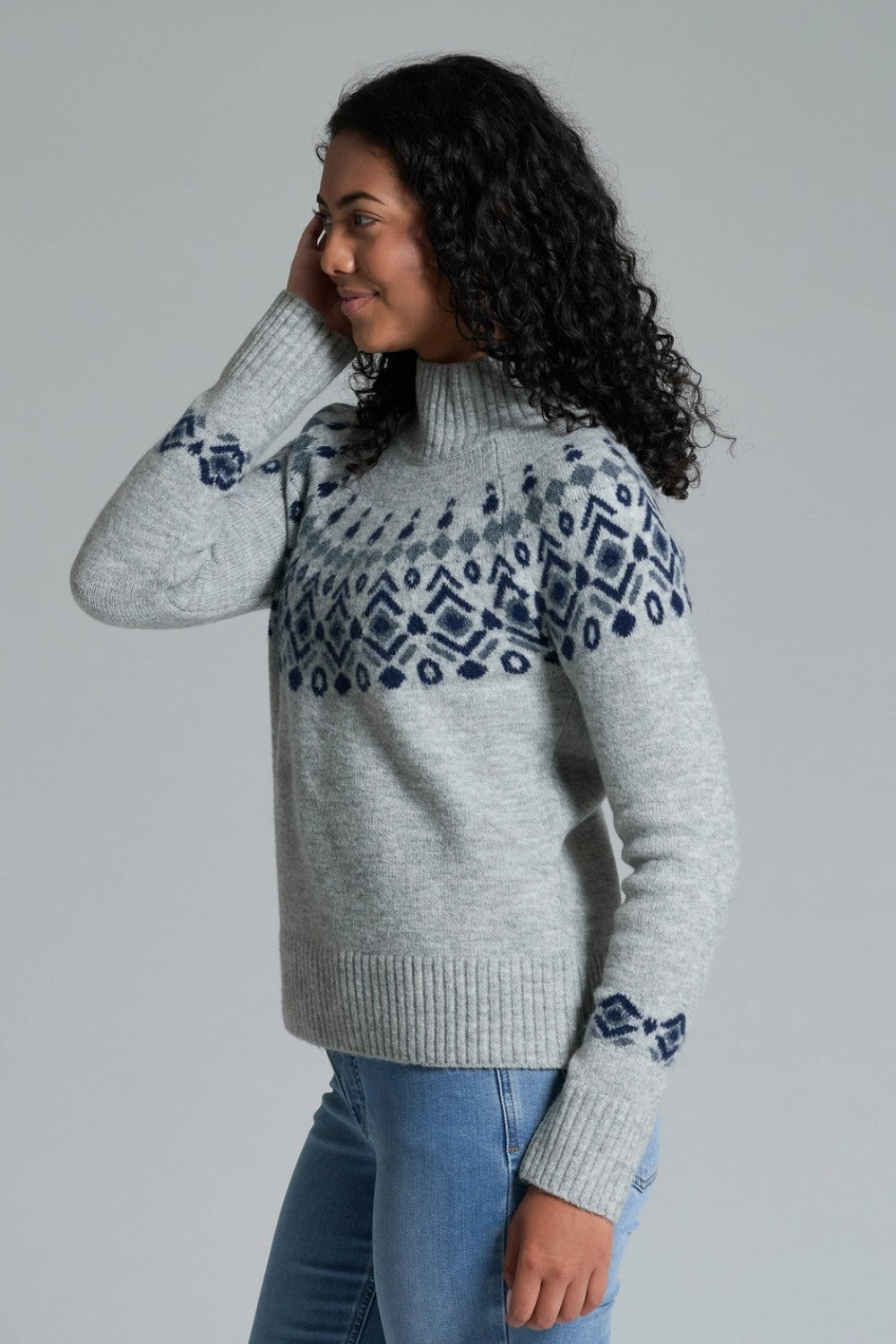Woman wearing a gray sweater with blue pattern against a plain background