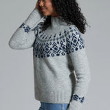 Woman wearing a gray sweater with blue pattern against a plain background