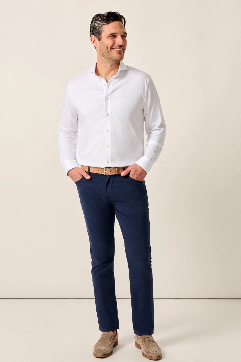 Man wearing a white dress shirt and navy pants against a beige background