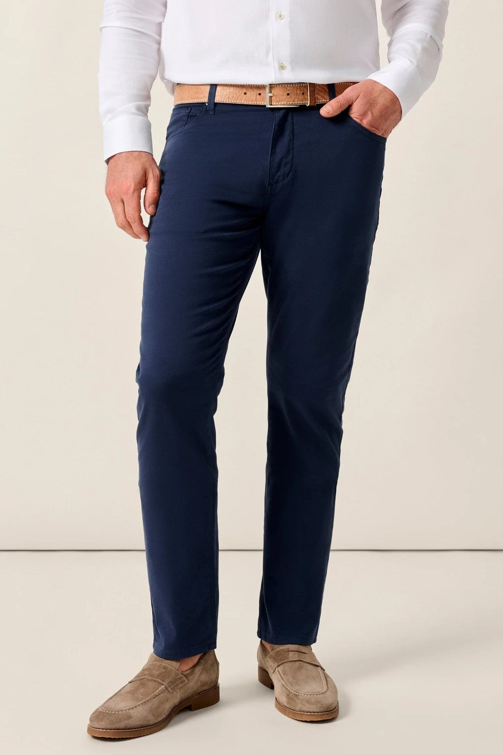 Person wearing navy pants with a white shirt and brown shoes on a beige background