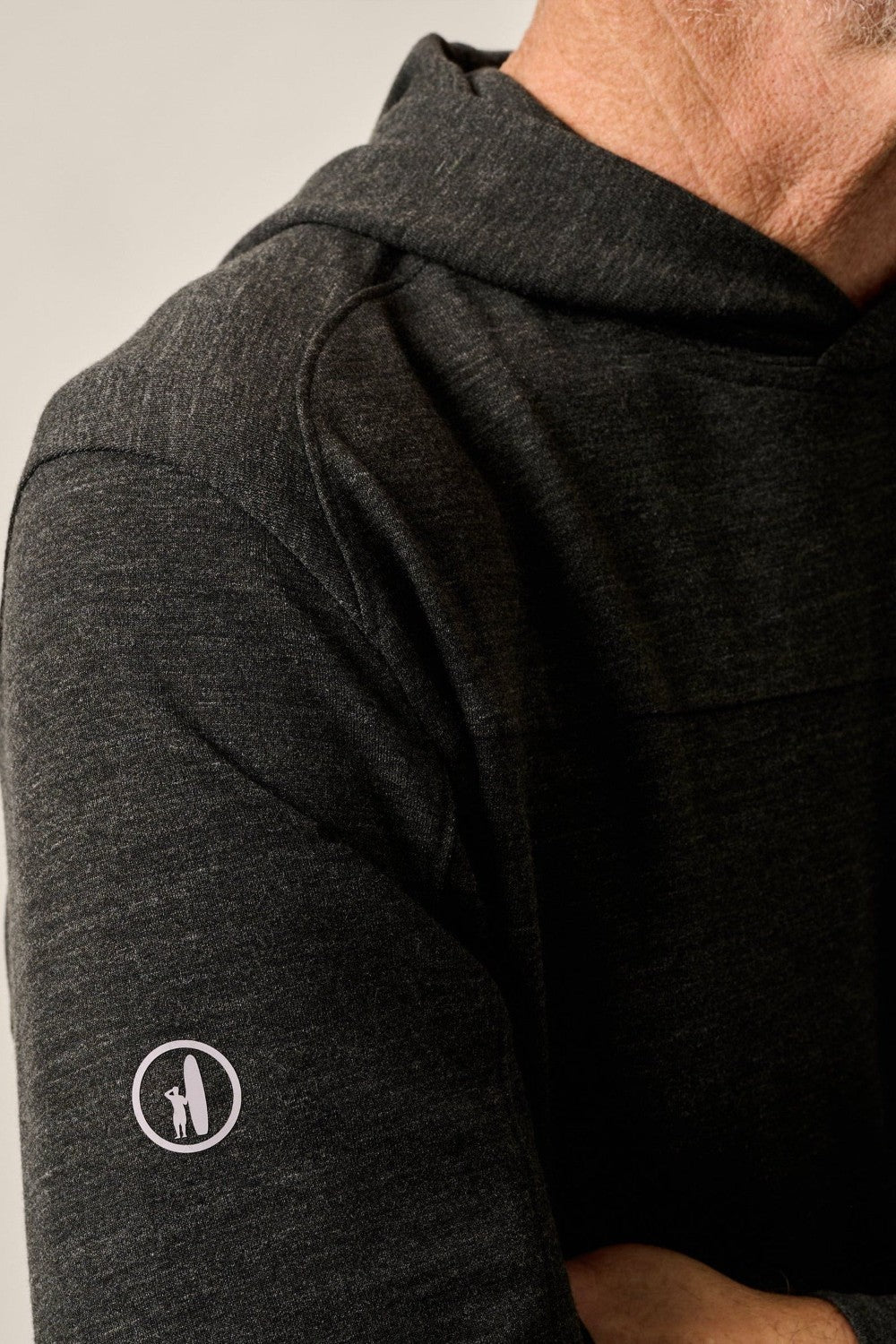 Close-up of a person wearing a dark gray long-sleeve shirt with a logo on the sleeve.