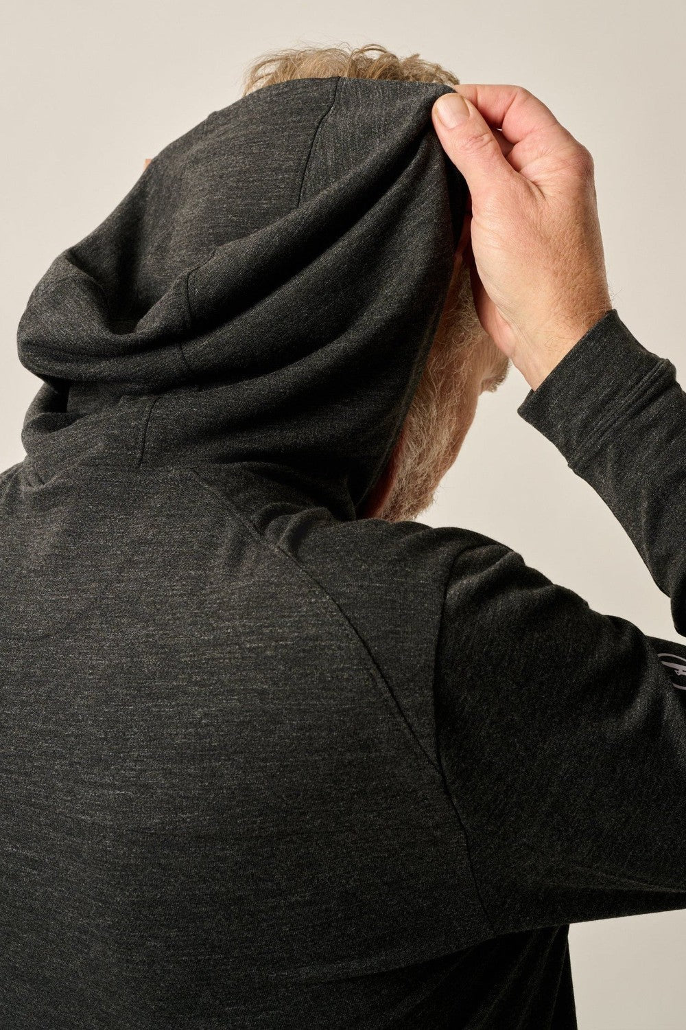Person wearing a dark gray hoodie adjusting the hood against a neutral background