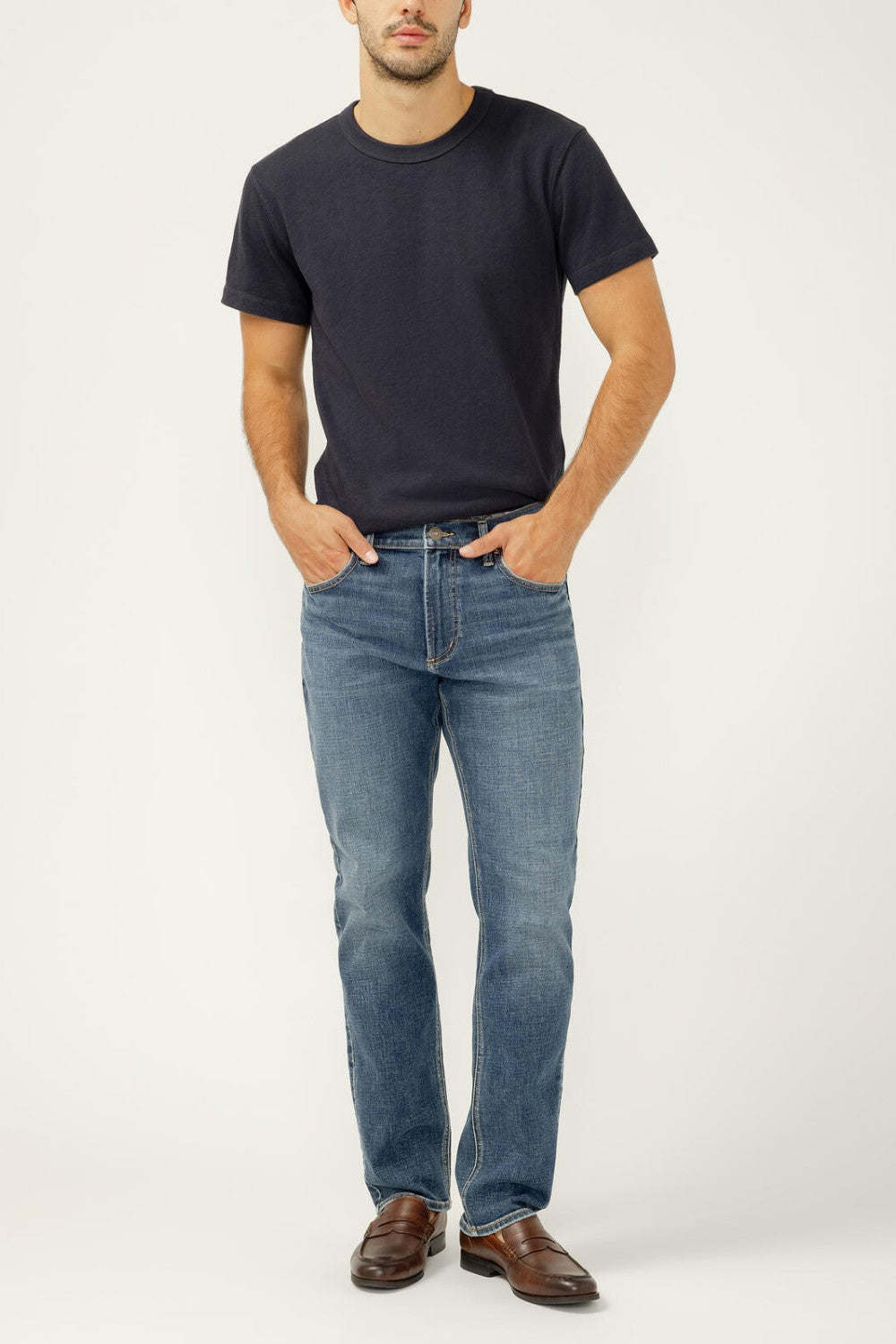 Man wearing a navy t-shirt and blue jeans on a white background