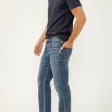 Man wearing a dark blue t-shirt and light blue jeans on a white background