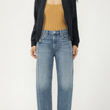 Woman wearing a black jacket, mustard top, and blue jeans on a white background