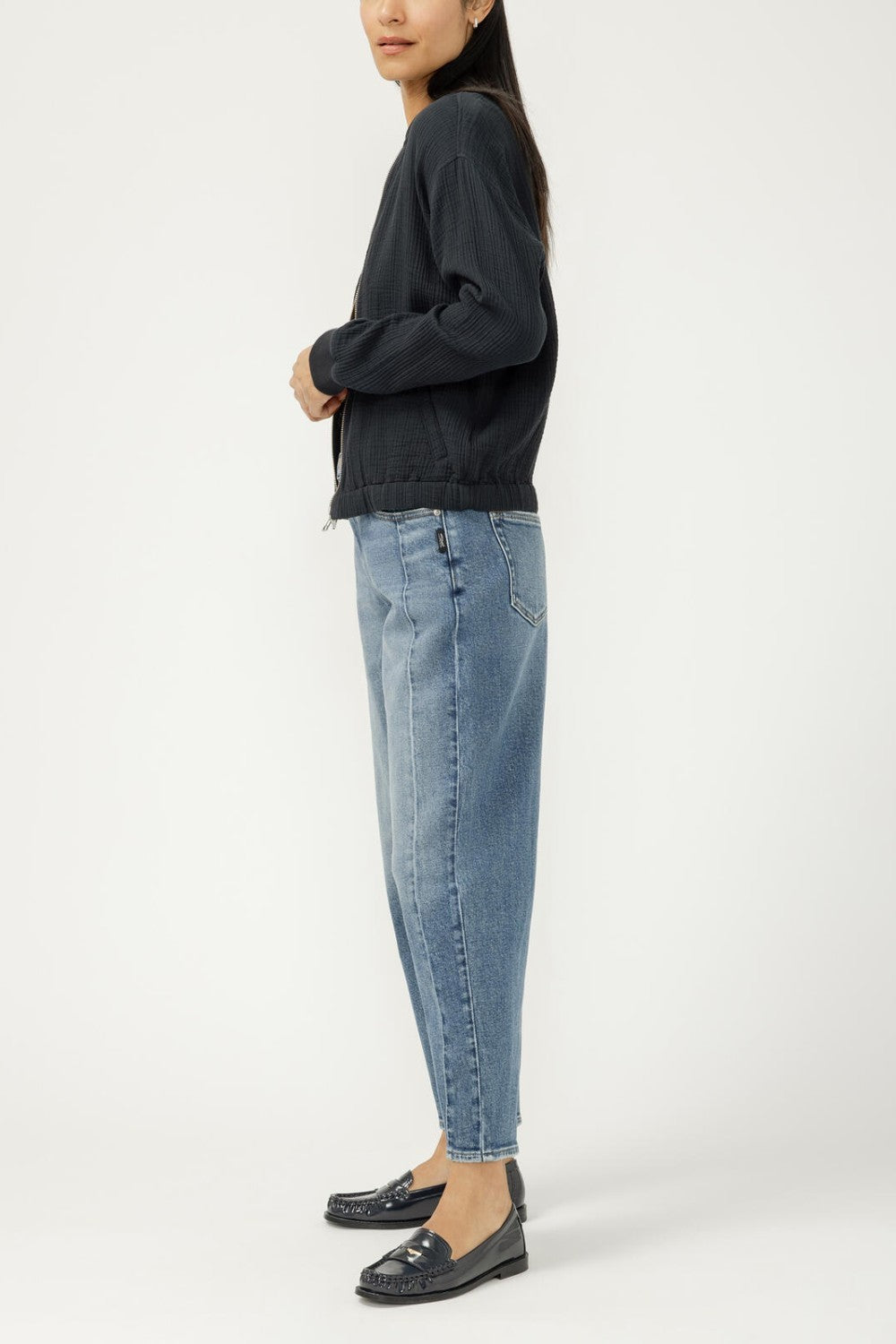 Person wearing a dark sweater and light blue jeans on a white background