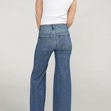 Person wearing blue jeans and a white top on a plain background