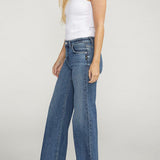 Woman wearing a white tank top and blue jeans on a plain background