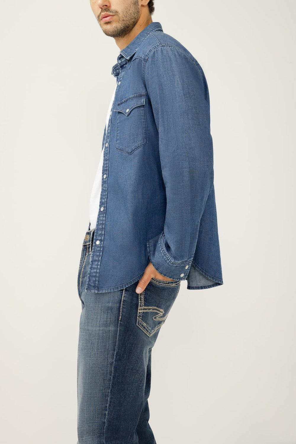 Man wearing a blue denim shirt and jeans on a white background