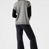 Woman wearing a gray sweater with black sleeves and black pants on a white background
