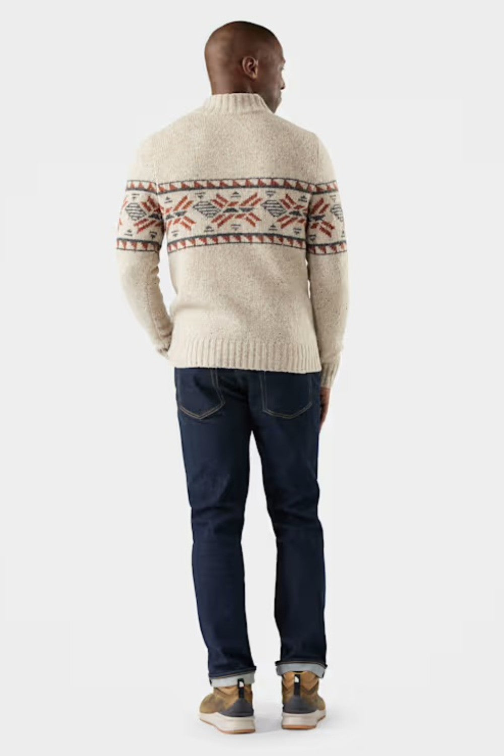 Man wearing a cream sweater with a pattern and dark jeans on a white background