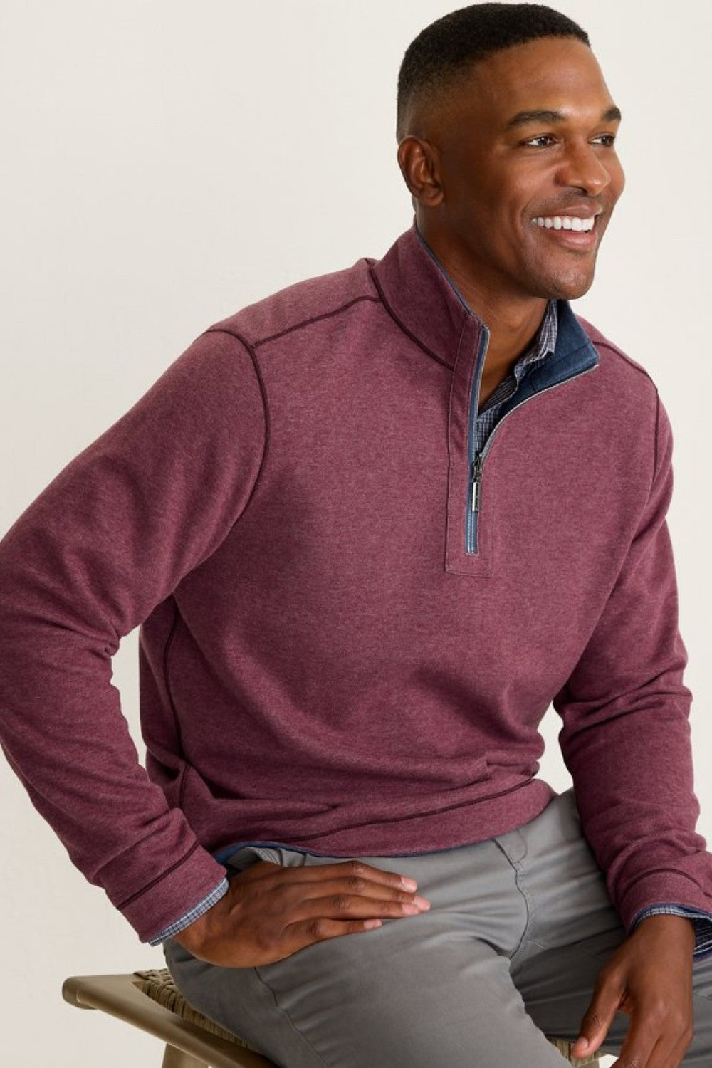 Man wearing a maroon pullover with a visible brand logo, sitting on a bench.