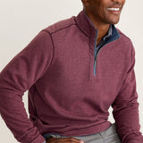 Man wearing a maroon pullover with a visible brand logo, sitting on a bench.
