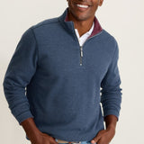 Man wearing a blue quarter-zip sweater with a white shirt underneath on a beige background