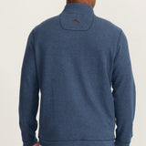 Person wearing a blue sweater with a visible brand logo on the back against a plain background