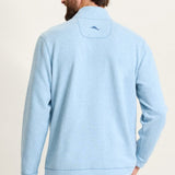 Man wearing a light blue pullover with a logo on the back against a plain background