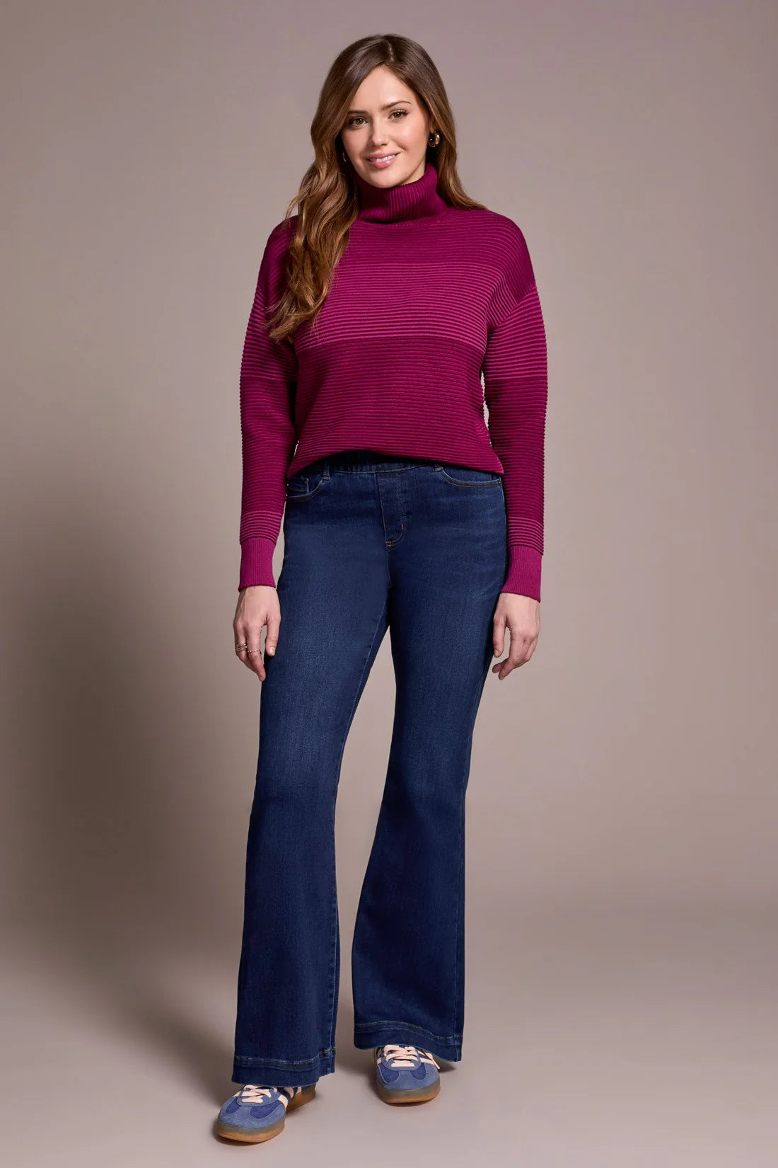 Woman wearing a magenta sweater and blue jeans against a beige background