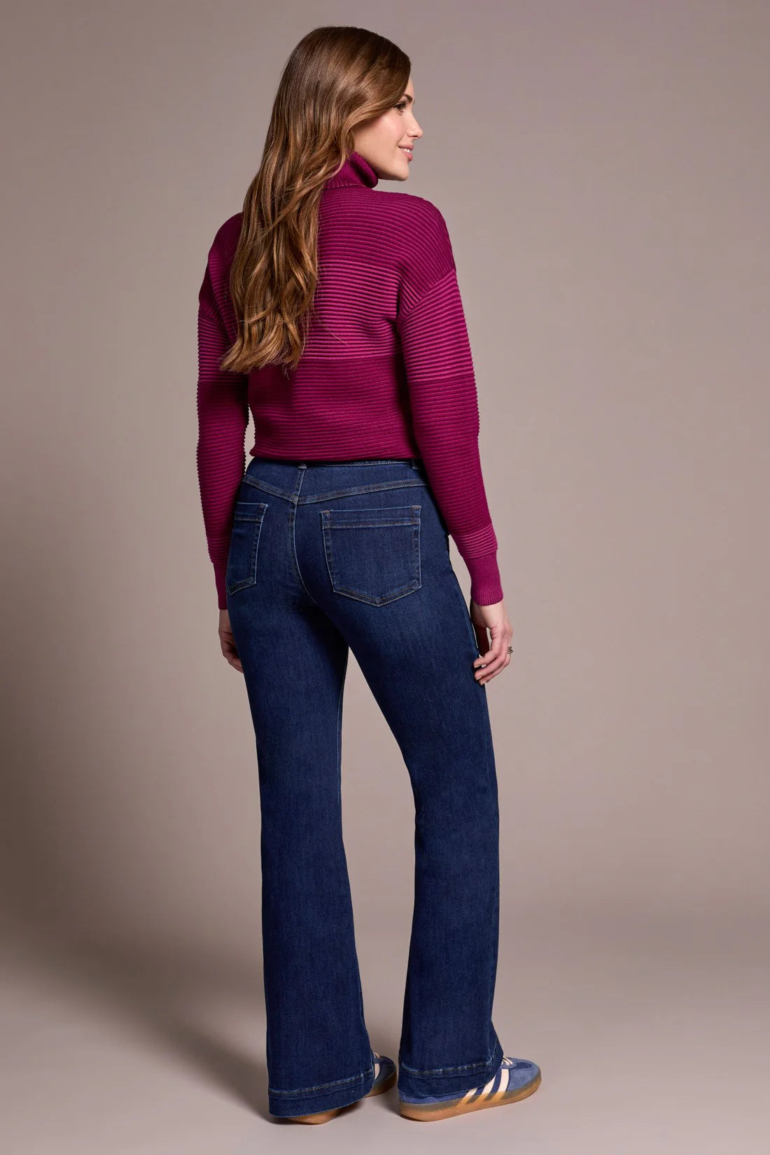 Woman wearing a magenta sweater and blue jeans against a beige background