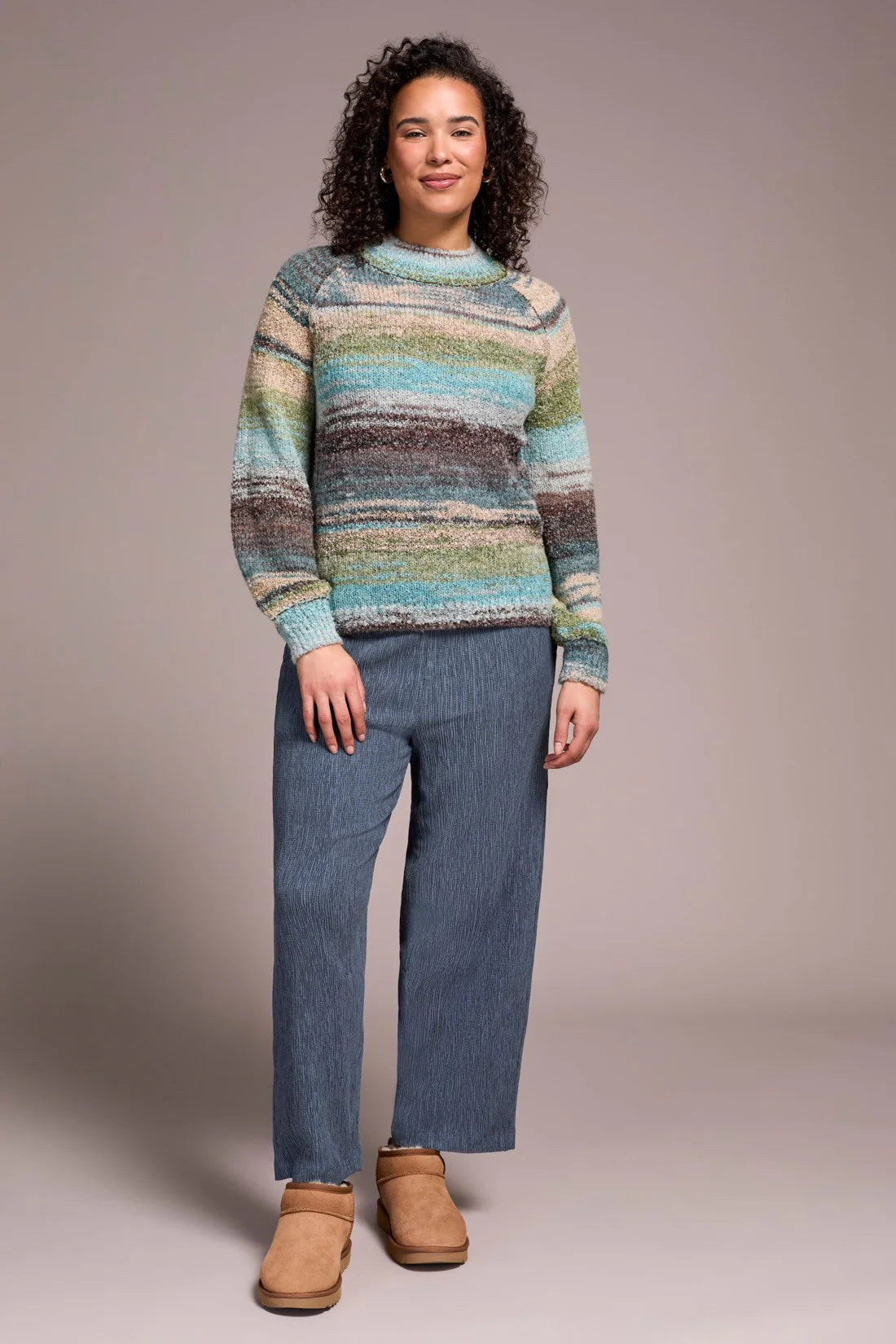 Woman wearing a colorful striped sweater and blue pants against a plain background