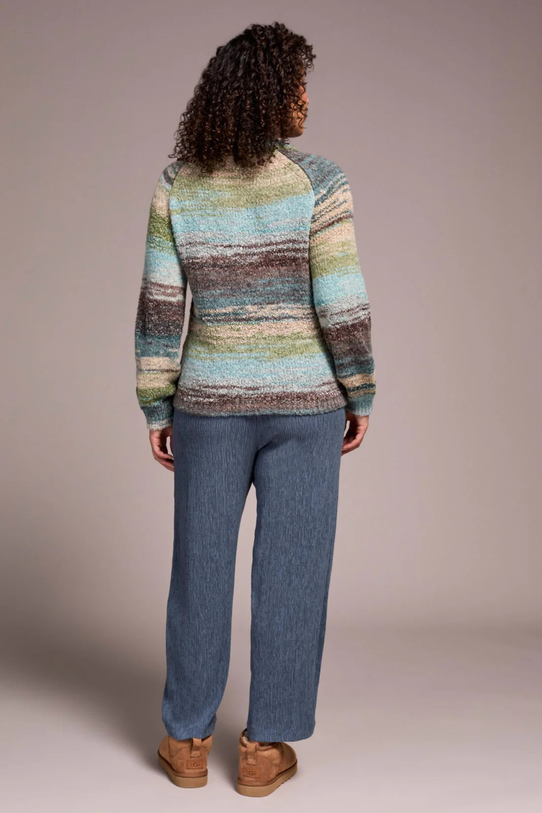Person wearing a multicolored striped sweater and blue pants on a plain background
