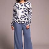 Woman wearing a patterned top and blue pants against a plain background