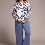 Woman wearing a patterned top and blue pants against a plain background
