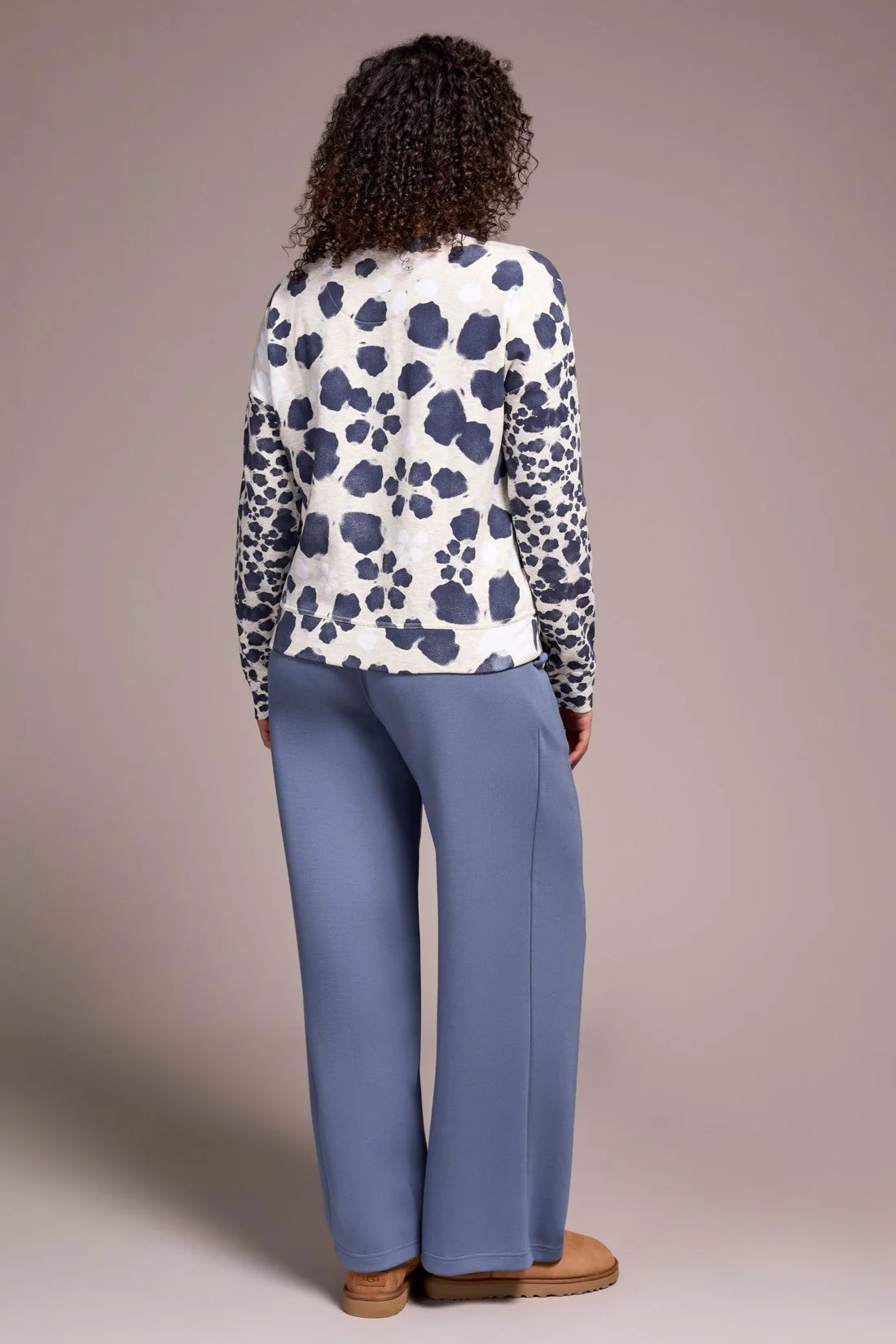 Person wearing a patterned top and blue pants against a beige background