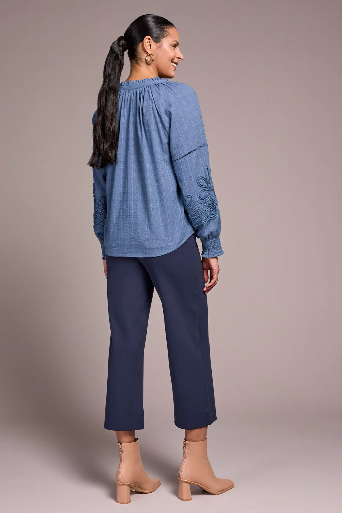 Woman wearing a blue embroidered blouse and pants on a plain background