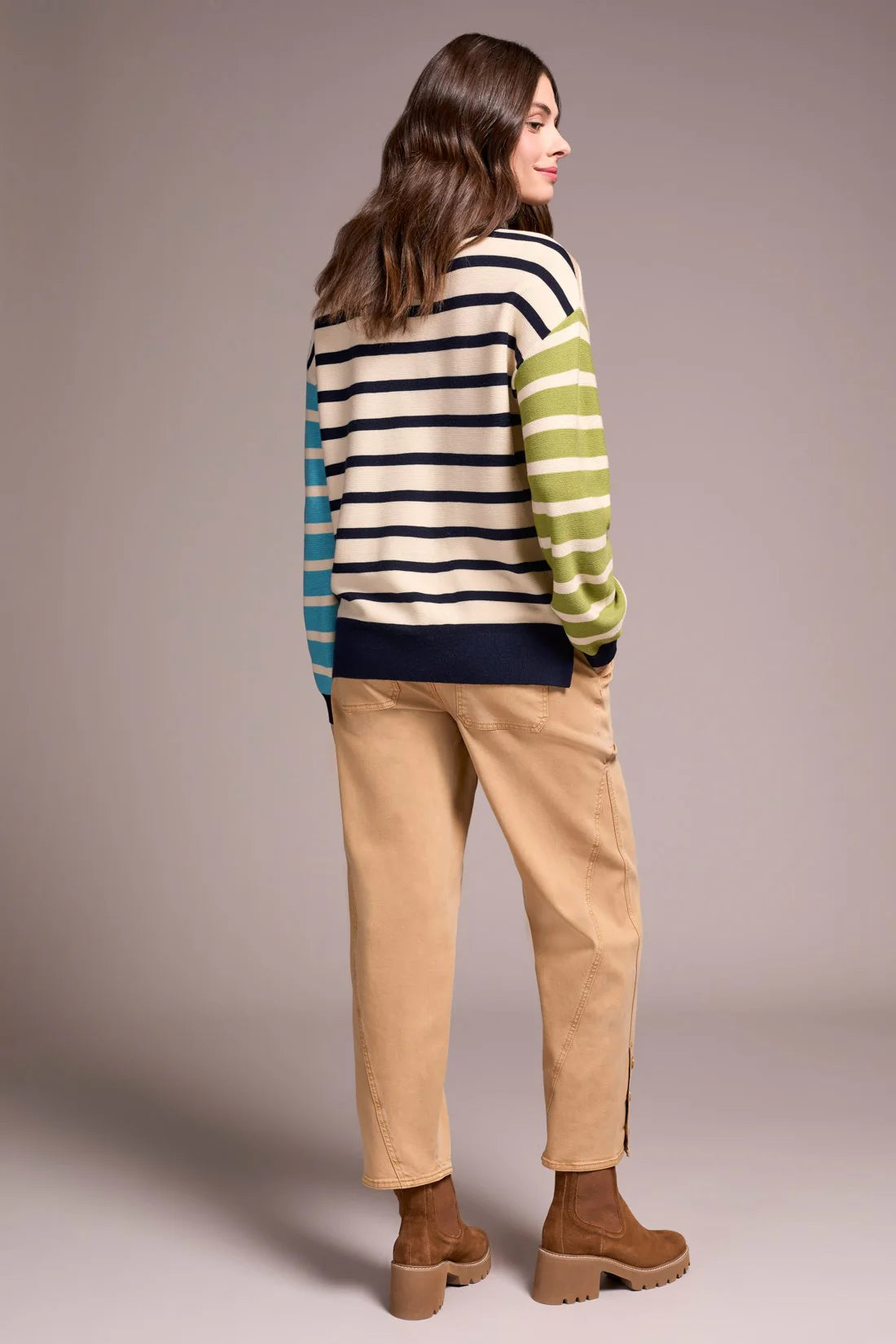 Woman wearing a striped sweater and beige pants against a plain background