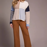 Woman wearing a striped sweater and brown pants against a plain background