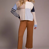 Woman wearing a colorful striped sweater and brown pants on a plain background