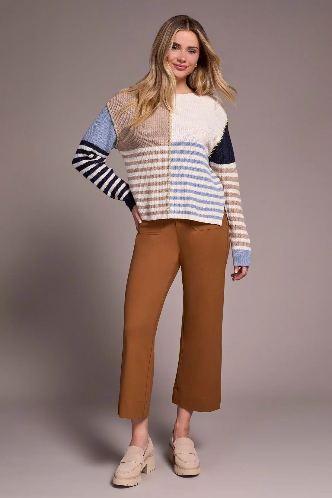 Woman wearing a colorful striped sweater and brown pants on a plain background