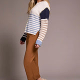 Woman wearing a striped sweater and brown pants against a plain background