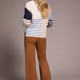 Woman wearing a colorful sweater and brown pants against a plain background