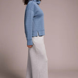 Woman wearing a blue sweater and gray pants against a plain background