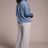 Woman wearing a blue sweater and gray pants against a beige background