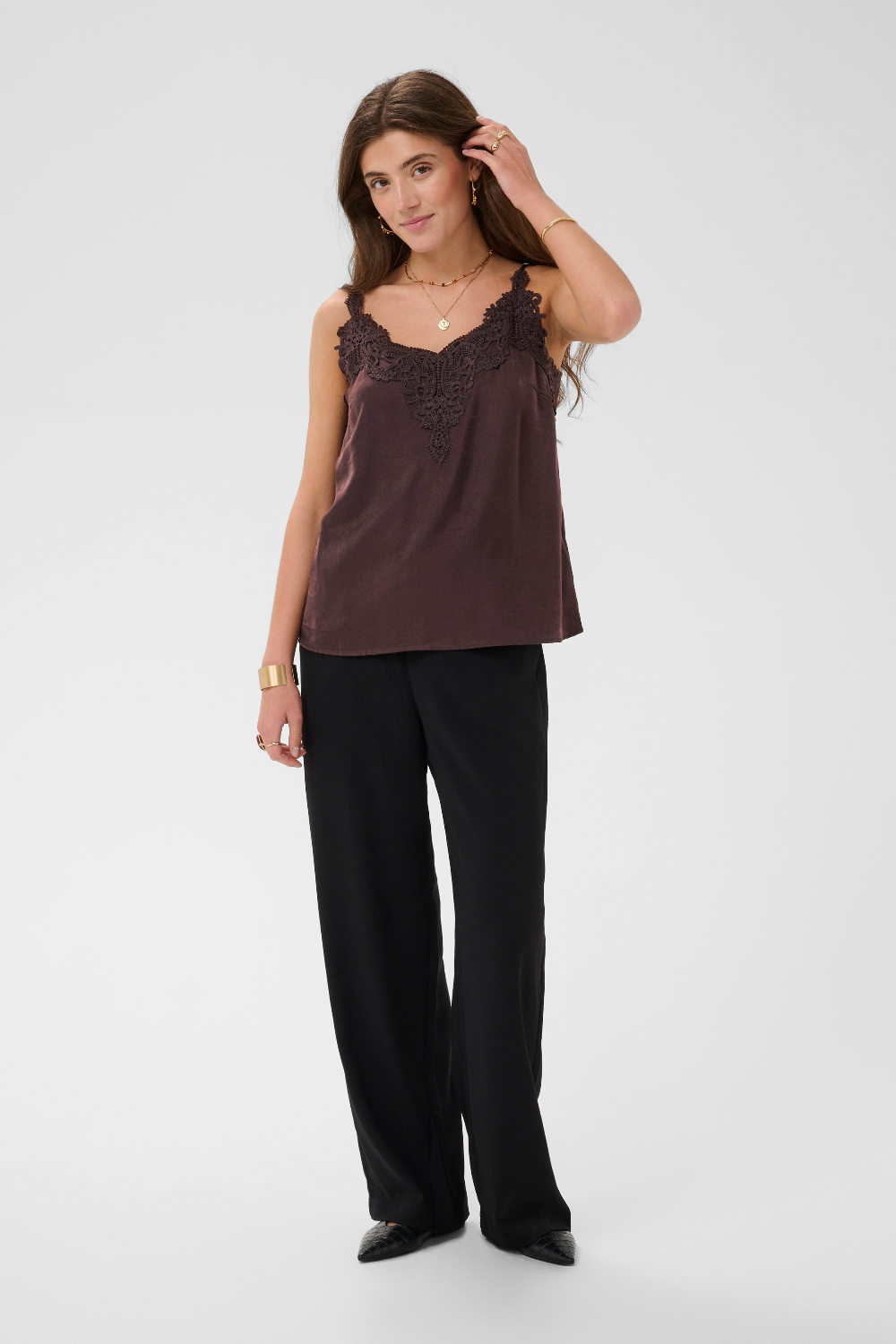 Woman modelling a brown camisole with black pants and black shoes photographed against a light backdrop.