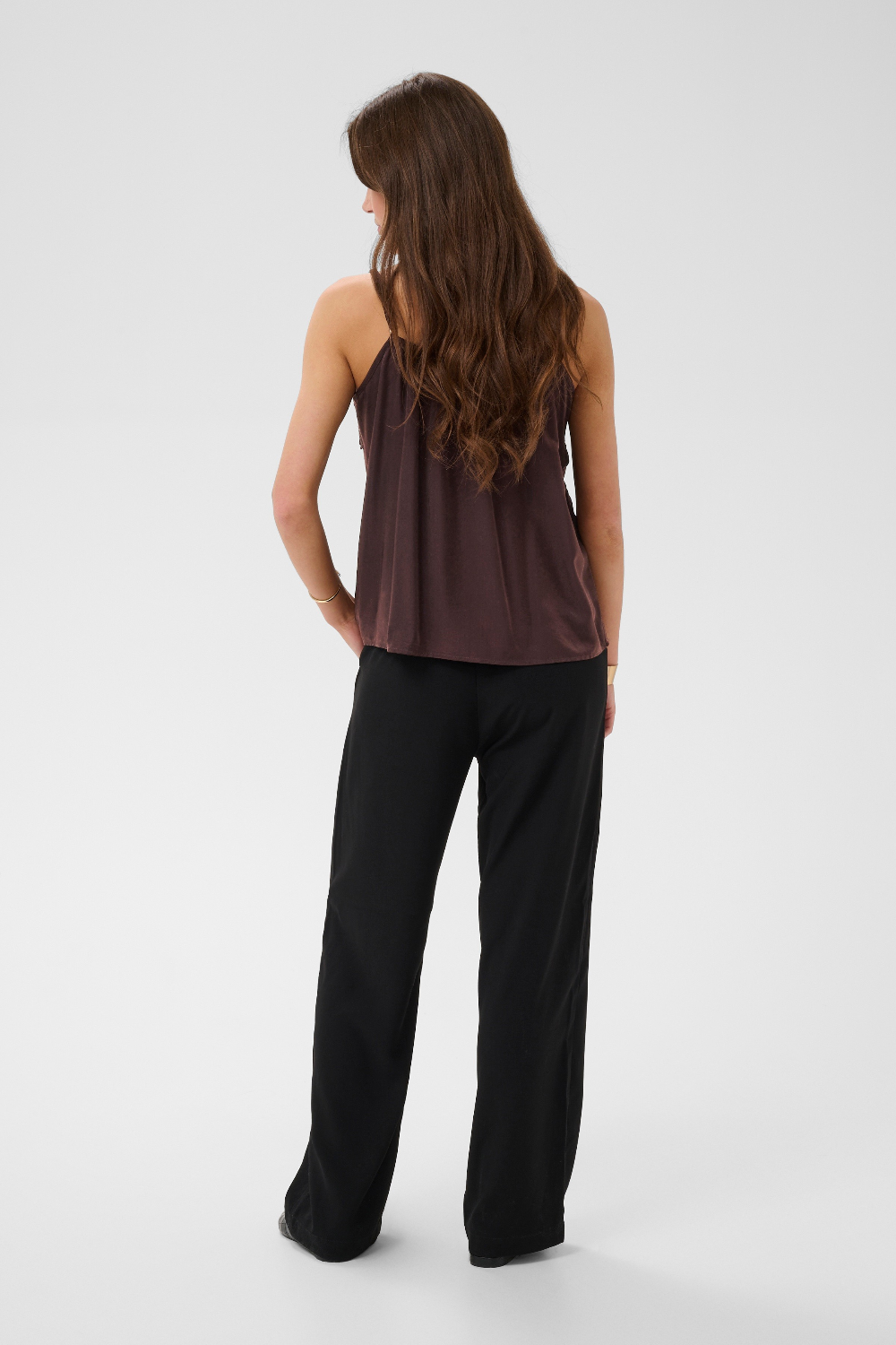 Woman, shown from behind, modelling a brown camisole with black pants photographed against a light backdrop.