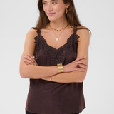 Woman modelling a brown camisole with black pants photographed against a light backdrop.