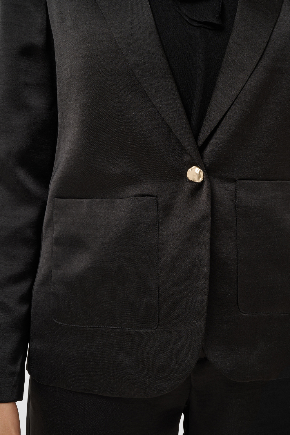 Close up of a black sateen suit with a black blouse photographed against a light background.