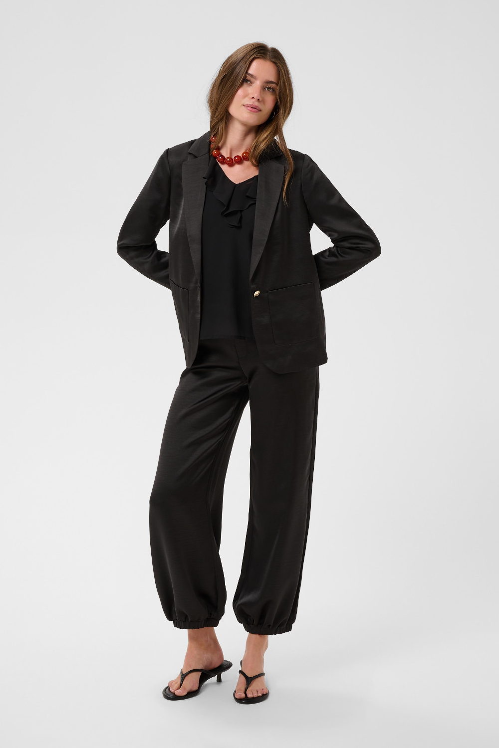 Women modelling a black sateen suit with a black blouse and black kitten heels photographed against a light background.
