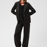 Women modelling a black sateen suit with a black blouse and black kitten heels photographed against a light background.